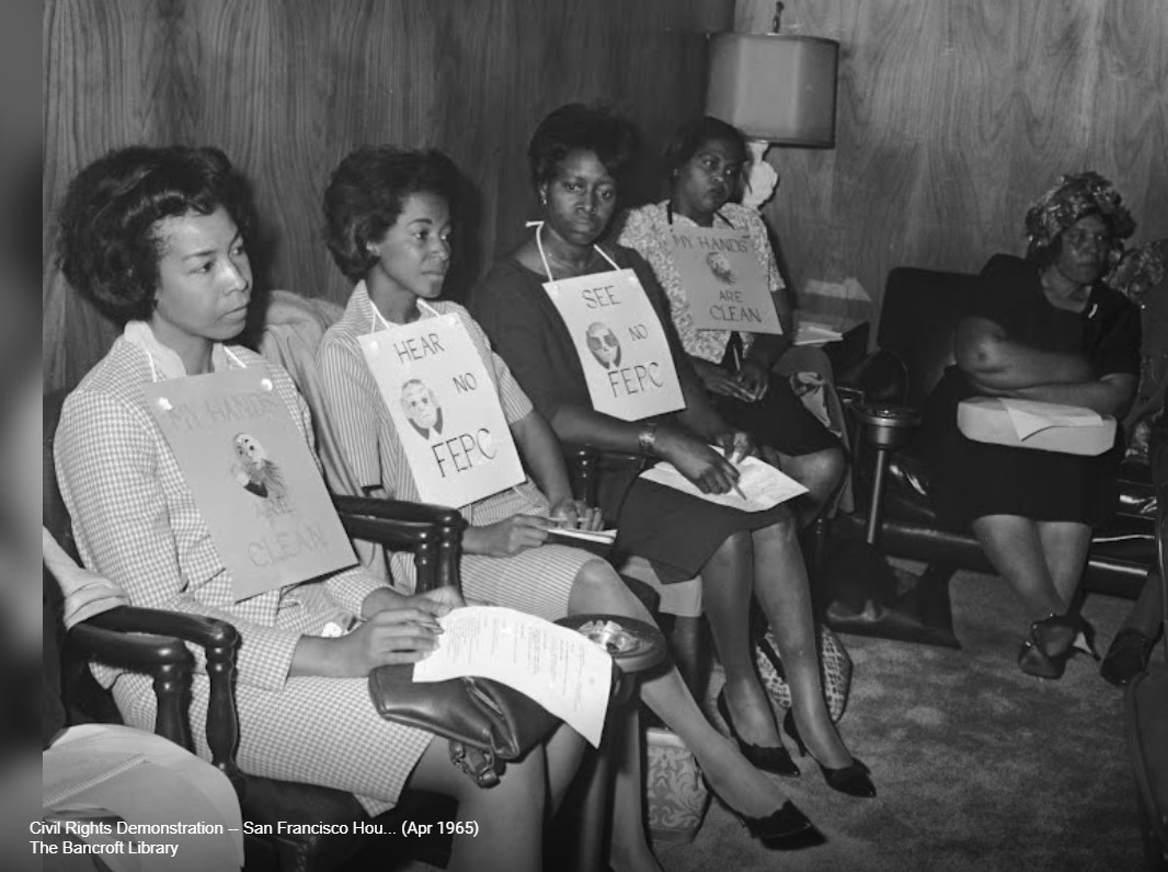 A group of African American woman sit in a Civil Rights Demonstration in 1965 wearing signs on their neck reading "Hear no FEPC."