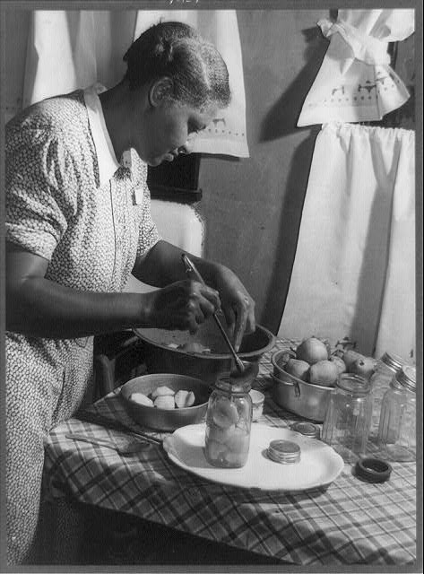 An old photograph, circa 1920s, of an African American cooking in a kitchen.