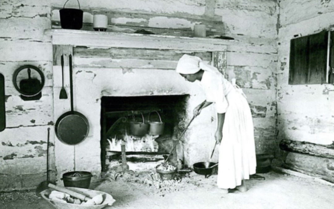An old photograph of an African American woman cooking food by a fireplace.