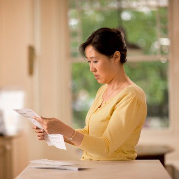 A parent reads documents from a stack of mail in their kitchen.