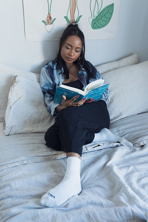 A woman reading a book sitting on a bed.